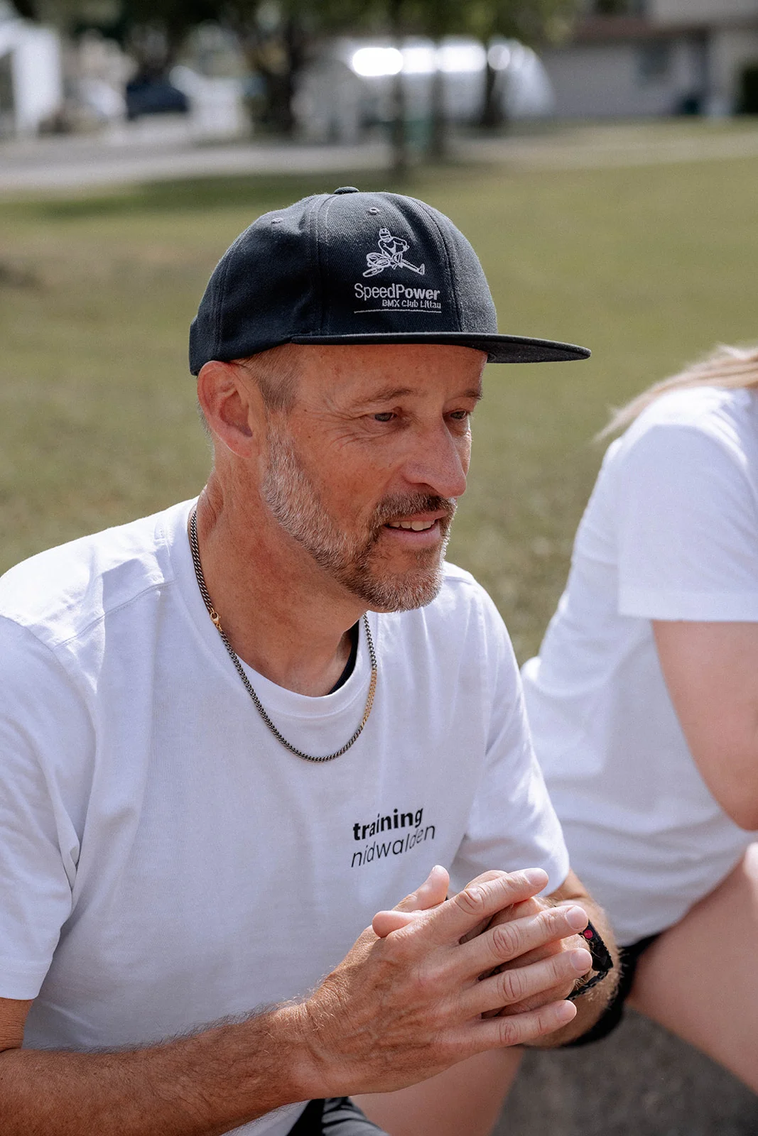 Hans-Peter wearing a cap, sitting on the wall in conversation