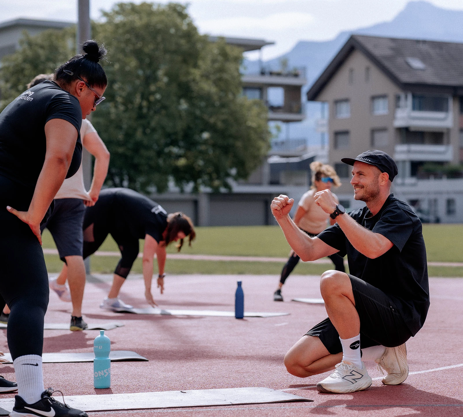 A training nidwalden coach cheering on a participant while the group stretches on the running track behind them