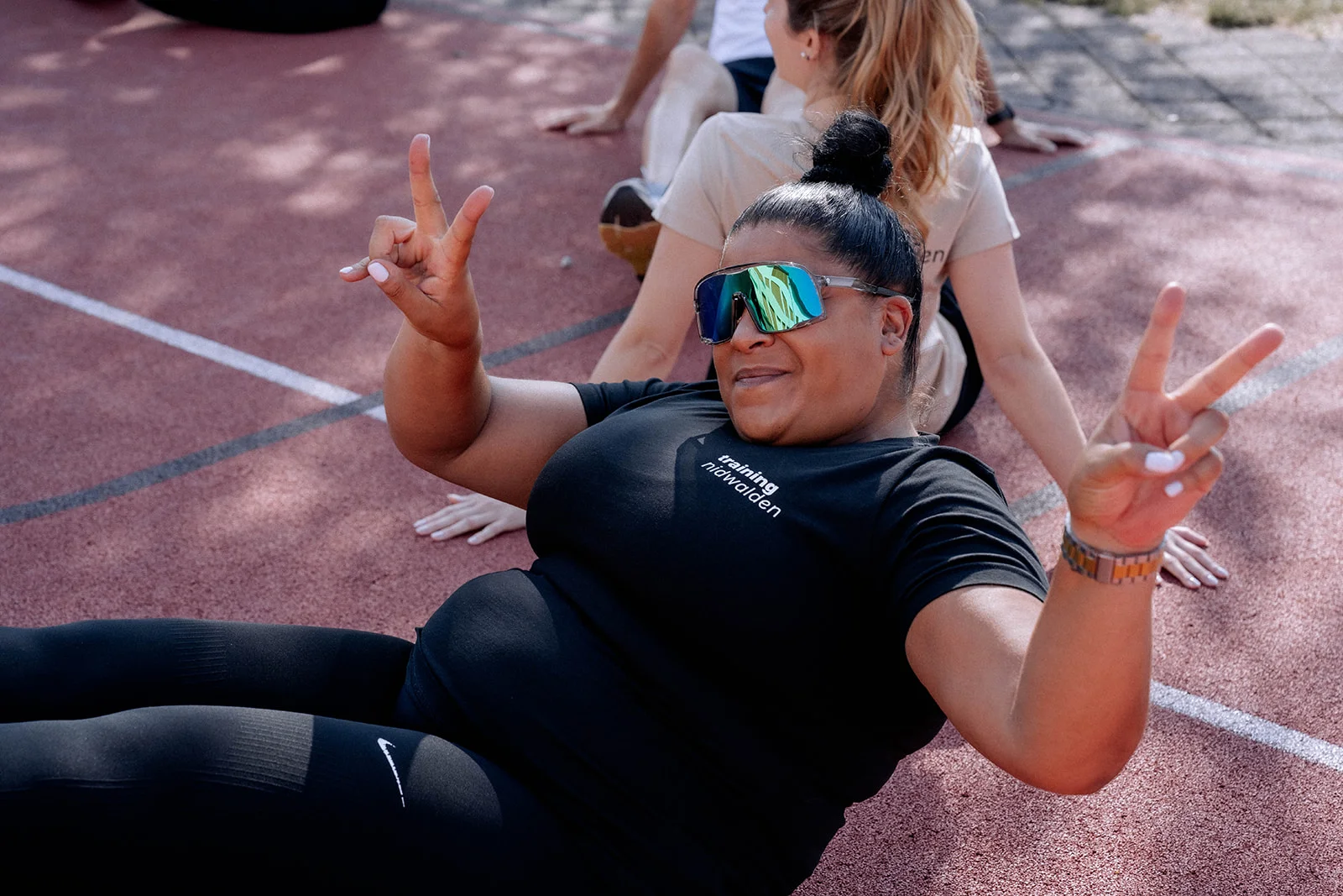 Pädle sitting on the running track, laughing and giving a peace sign
